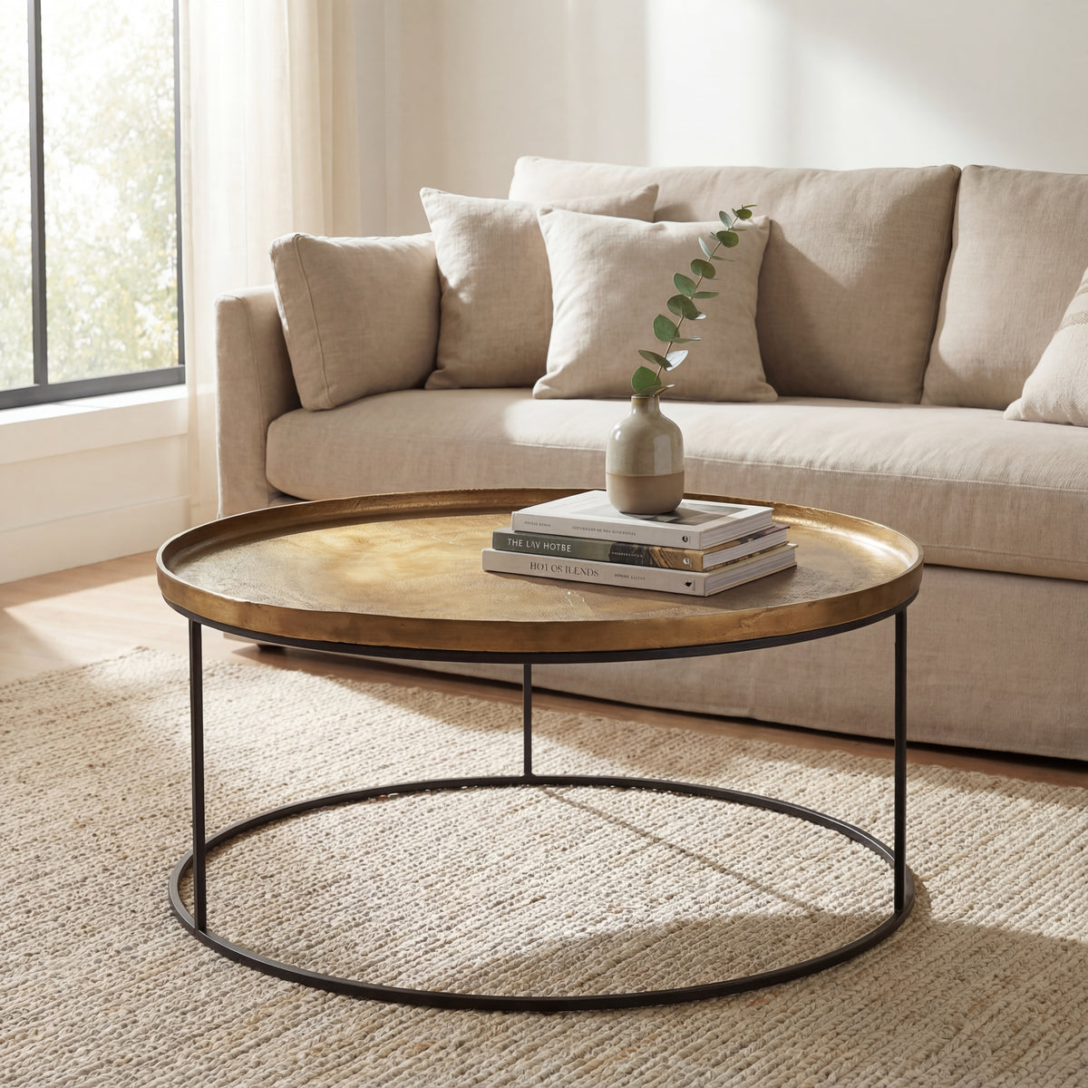 Sana Coffee Table by Urbia — round reclaimed-aluminum table styled before a beige sofa in a bright living room