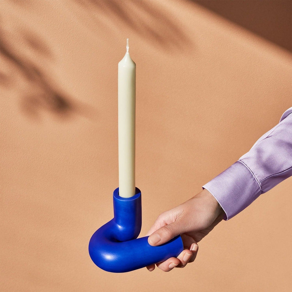 OCTAEVO Templo blue candle holder held by its curved base with a cream taper candle.