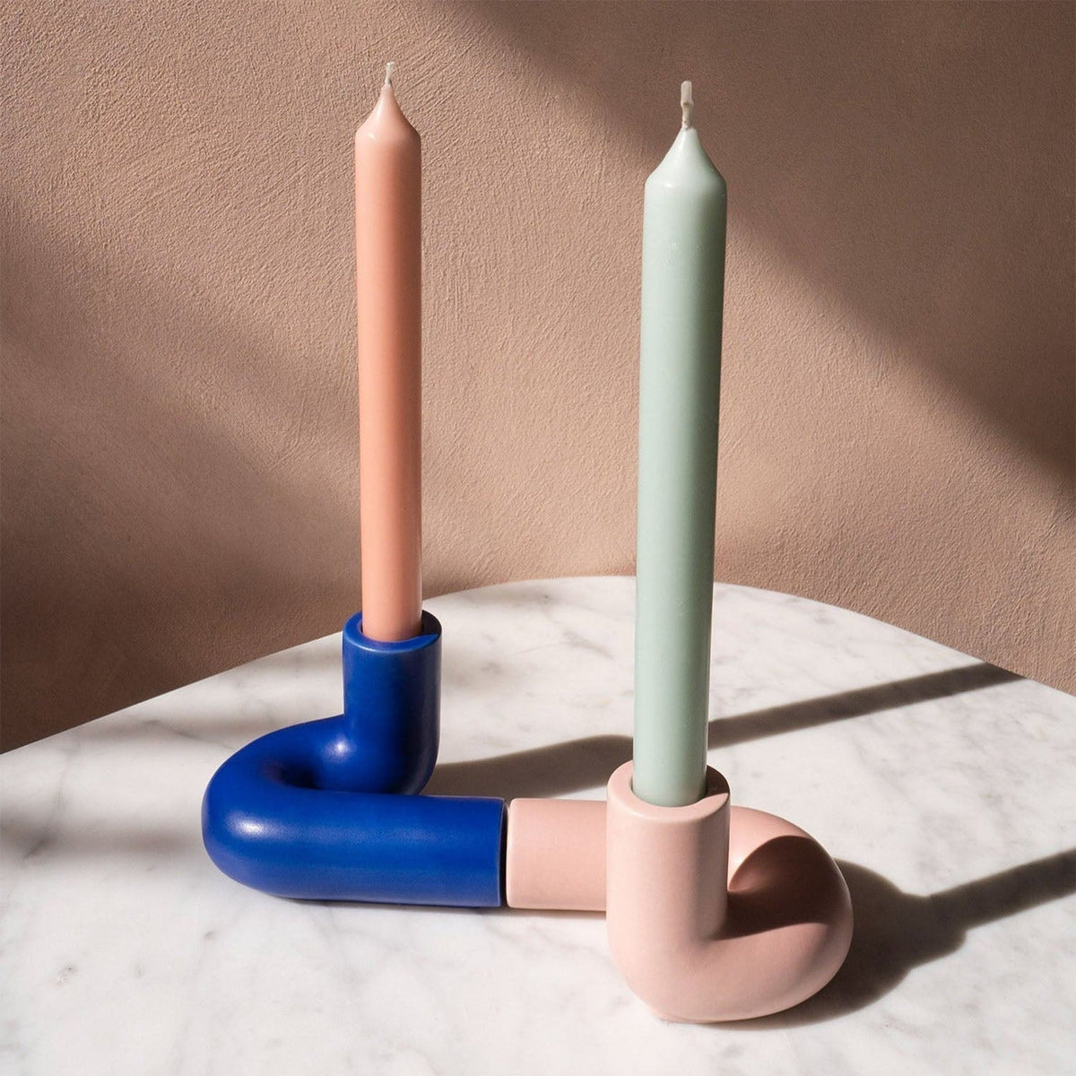 Blue OCTAEVO Templo Candle Holder paired with a pink holder and taper candles on a marble tabletop.
